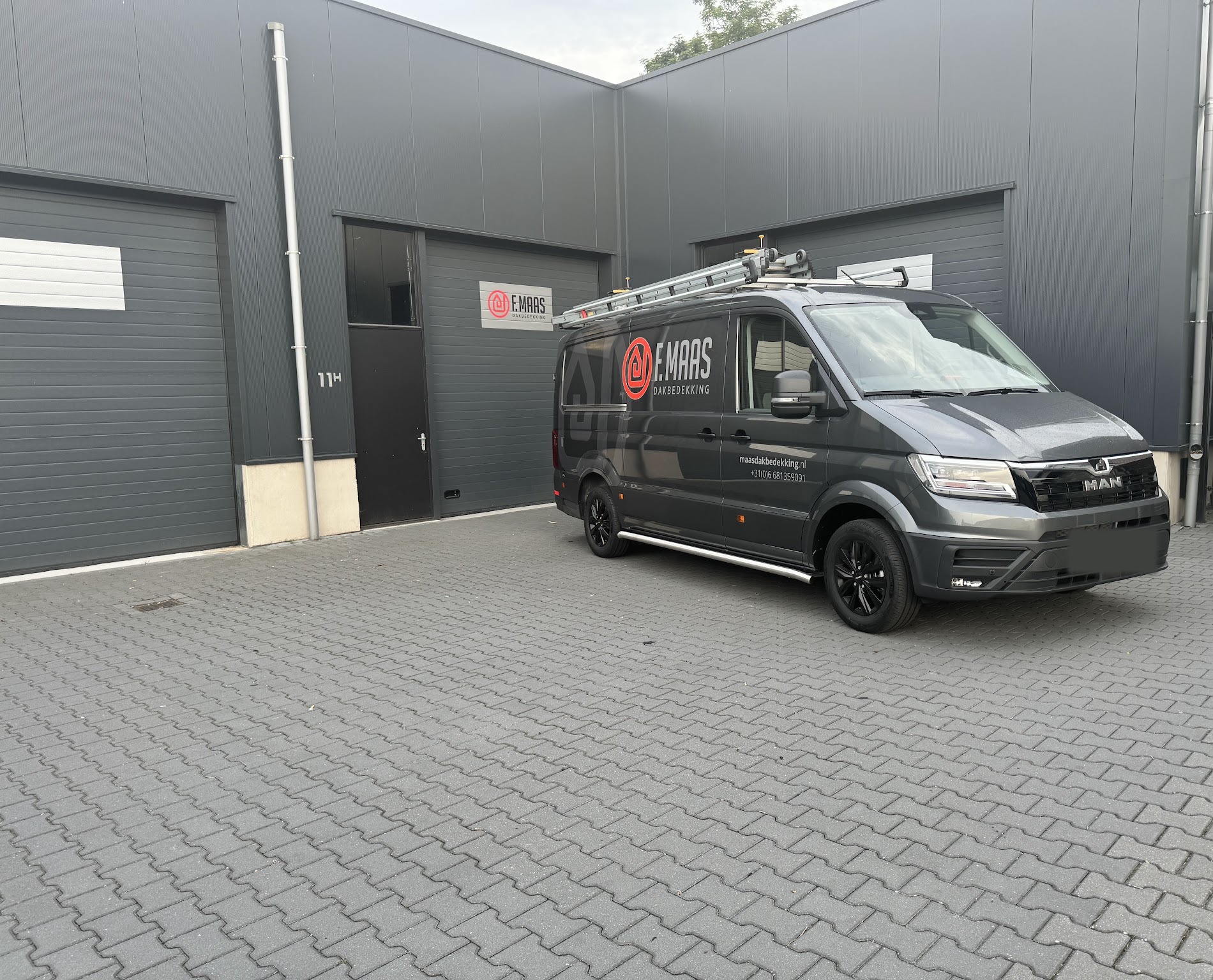 De grijze bedrijfsbus van F. Maas Dakbedekking voor de bedrijfsunit met het logo op de deur