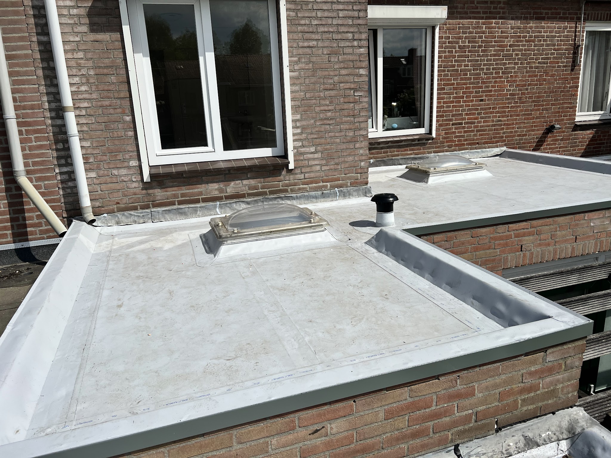 Nieuwe kunststof dakbedekking met lichtkoepel en ontluchting op een aanbouw tegen een bakstenen woning