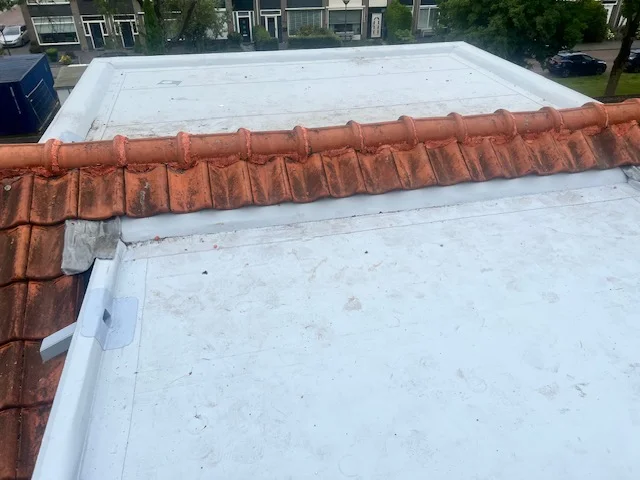 Wit kunststof plat dak aansluitend op een oranje pannendak